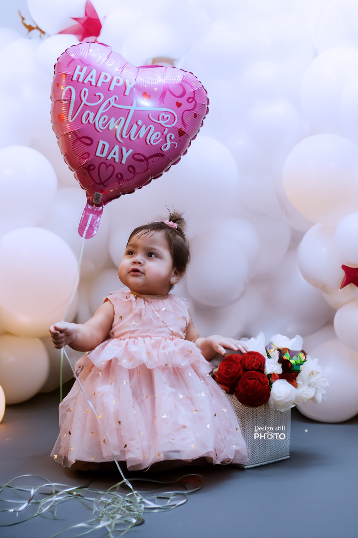 Baby girl in a pink dress with a Valentine balloon